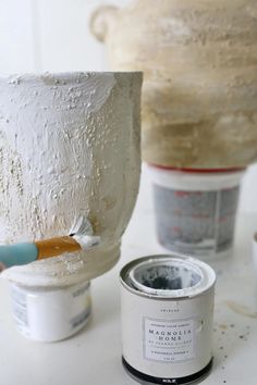 two pots with white paint and one has a brush in it