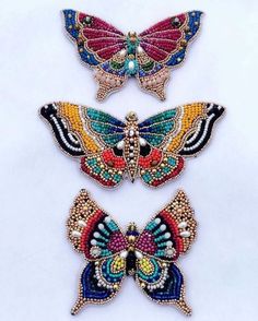 three butterflies made out of beads on a white surface with one butterfly in the middle