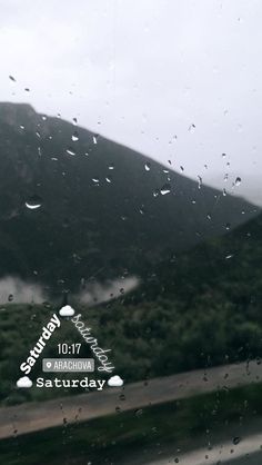 rain drops on the windshield of a car as it drives down a road in front of a mountain