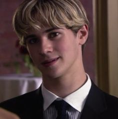 a young man in a suit and tie looking at the camera while he is talking to someone