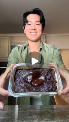 a man holding up a chocolate cake in a glass dish on top of a counter