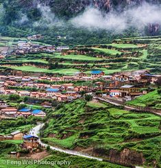 an aerial view of a village surrounded by lush green fields and mountains in the distance