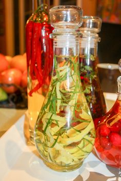 three glass jars filled with different types of vegetables and herbs on a table top next to fruit