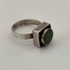 A modernist bezel style ring by Erik Granit & Co from Finland. The ring is sterling silver with patina highlights and features a green stone. 3.6 grams Size 5 but can be easily resized by a reputable jeweler Hallmarks: 925 Sterling Finland, V7 (1974), designer's hallmark Modern Green Collectible Jewelry, Modern Green Cabochon Rings, Modernist Sterling Silver Rings, Green Modernist Rings For Anniversary, Modernist Green Rings For Anniversary, Modernist Green Ring For Formal Occasions, Contemporary Green Sterling Silver Jewelry, Modern Green Cabochon Jewelry, Modern Cabochon Emerald Ring