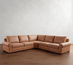 a tan leather couch sitting on top of a hard wood floor next to a white wall