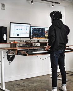 a person wearing headphones standing in front of a desk with two computer monitors on it