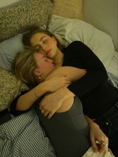 two women laying on top of a bed next to each other with their arms around each other