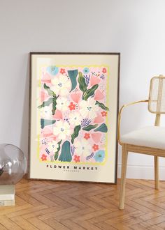 a framed flower market poster sitting on top of a wooden floor next to a chair