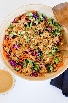 a bowl filled with shredded carrots and coleslaw next to a wooden spoon