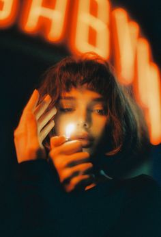 a woman is holding her hand up to her face and looking at the light in front of her