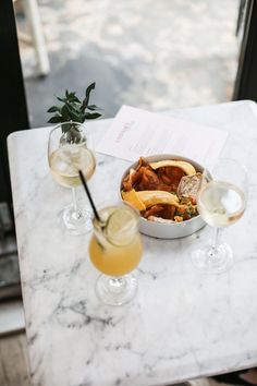 three glasses of wine on a marble table with food and drinks in front of them