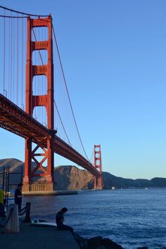 the golden gate bridge is seen from across the water with people sitting on rocks near it