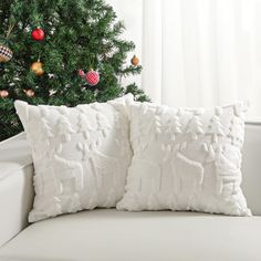 two white pillows sitting on top of a couch next to a christmas tree