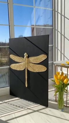 a vase filled with yellow flowers sitting next to a black and gold dragonfly art piece