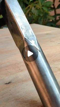 a metal object sitting on top of a wooden table next to a plant in the background