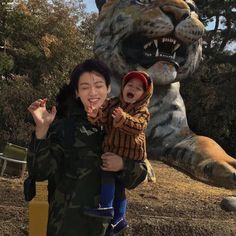 a woman holding a child in front of a statue of a tiger with its mouth open