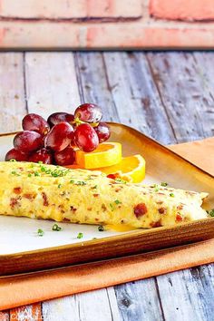 an omelet with grapes and oranges on a wooden tray next to a glass of water