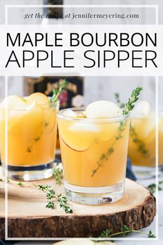 two glasses filled with maple bourbon apple cider on top of a wooden board and surrounded by greenery