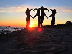 four people holding hands in the shape of heart on beach with sun setting behind them