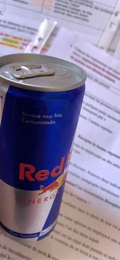 a can of red bull energy drink sitting on top of a table next to papers