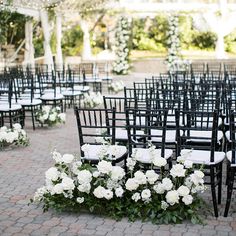 rows of black chairs with white flowers and greenery on the back are set up for an outdoor ceremony