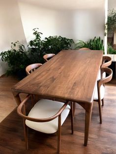 a wooden table with white chairs and plants on the wall in an empty room next to it