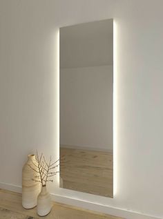 a white vase sitting next to a mirror on top of a hard wood floored floor