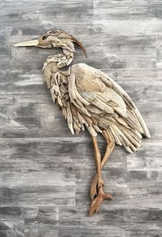 a bird made out of drift wood sitting on top of a wooden floor next to a wall