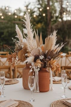 an arrangement of dried flowers in a vase on a table with place settings and wine glasses