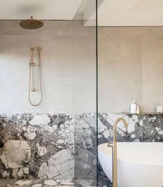 a bathtub and shower in a bathroom with marbled walls, flooring and gold fixtures