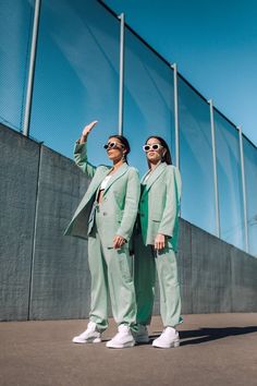 two women in light green suits and white shoes standing next to each other with their hands up