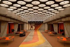 an empty room with orange chairs and round lights on the ceiling is shown in this image