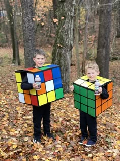 two young boys holding up rubik cubes in the woods with autumn leaves on the ground