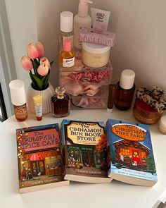 three books sitting on top of a white counter next to bottles and containers filled with cosmetics