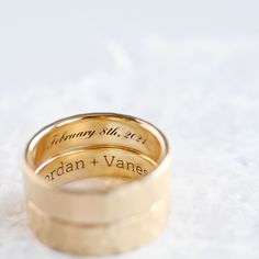 two gold wedding rings with names engraved on the sides, set against a white background