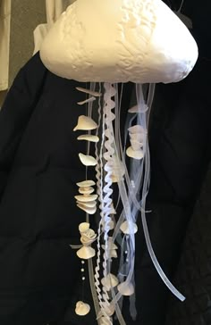 a large white jellyfish hanging from the side of a black jacket with shells attached to it