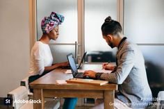 a man and woman sitting at a table working on their laptops, one is wearing a turban