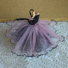 there is a small doll in a dress on the lace doily with a black shoe