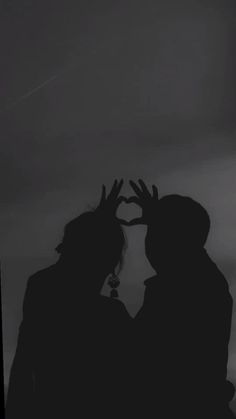 two people are standing in the dark with their hands up to make a heart shape