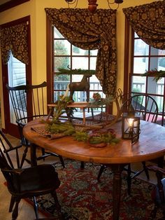 a wooden table with chairs around it in front of two windows and a rug on the floor