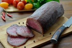 sliced meat sitting on top of a wooden cutting board next to vegetables and a knife