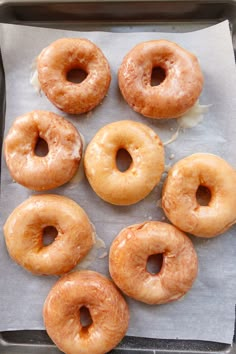 six glazed donuts sitting on top of a piece of wax paper in a pan