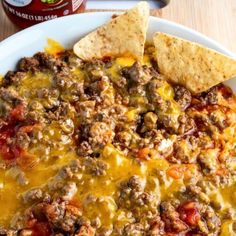 a white plate topped with cheese and tortilla chips next to a bottle of salsa