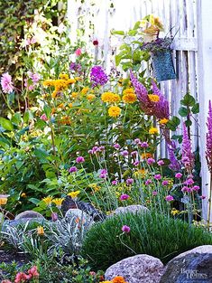 a garden filled with lots of flowers next to a white picketed fence and rocks