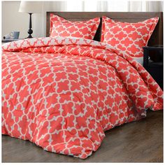 an orange and white comforter set with pillows on the bed in front of a window