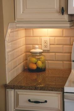 a kitchen with white cabinets and granite counter tops, along with a glass jar filled with fruit