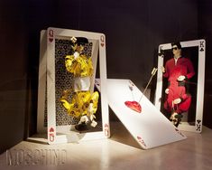 two mannequins dressed in costumes stand next to playing cards on a table