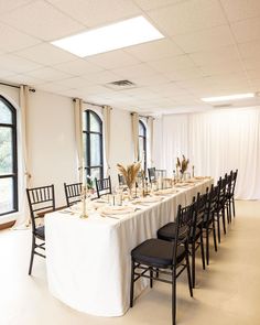 a long table is set up with black chairs and white linens for an event