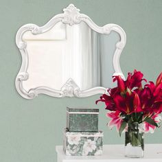 a vase filled with red flowers sitting on top of a table next to a mirror