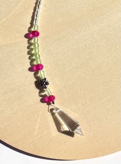 a necklace with pink and green beads hanging from it's side on a table